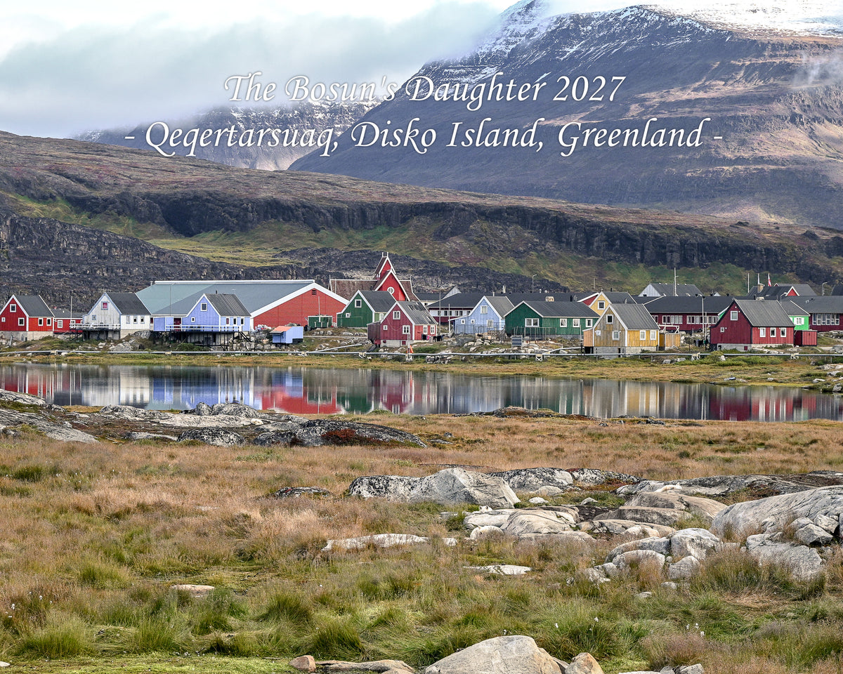 Disko Island 2027 calendar cover: the painted houses of Qeqertarsuaq beneath basalt mountains, Greenland